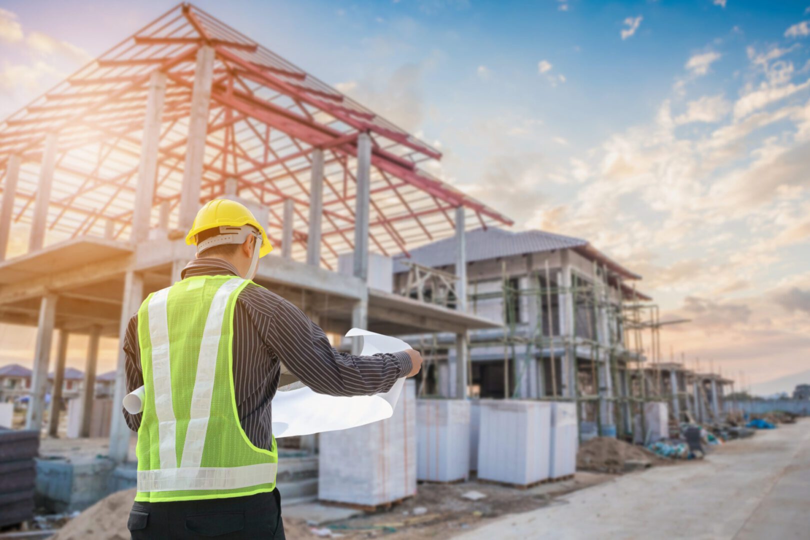 Construction worker reviewing plans at a building site during sunset.