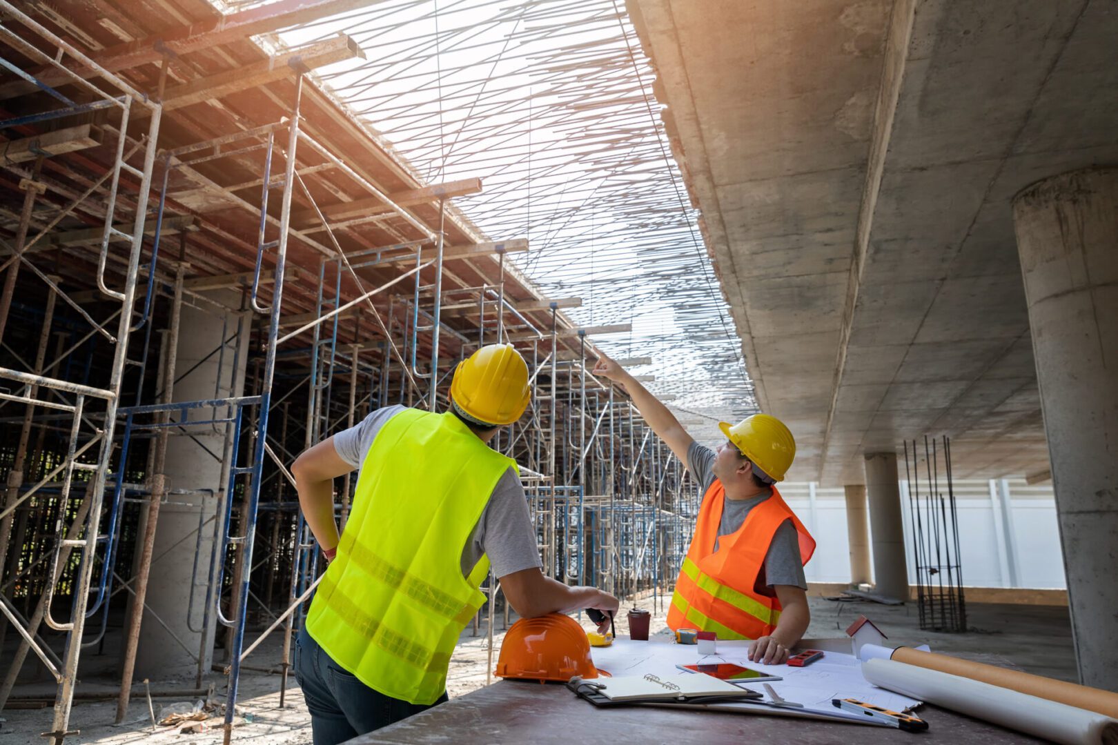 Construction workers discussing plans under a building framework.