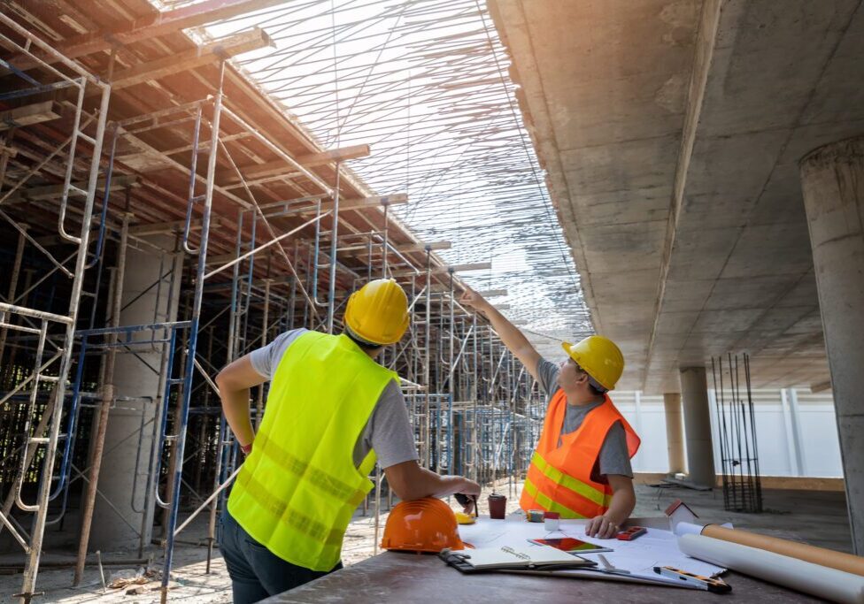 Construction workers discussing plans under a building framework.